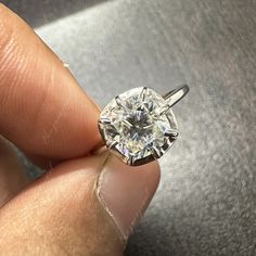 a close up of a person's hand holding a ring with a diamond in it