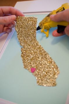 someone is cutting out the state shape from glitter paper with a pair of yellow scissors