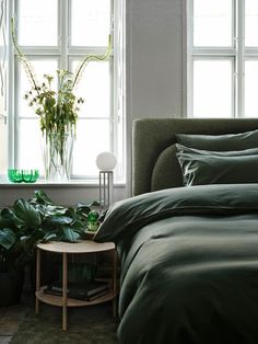 a bed with green sheets and pillows next to a plant in a window sill