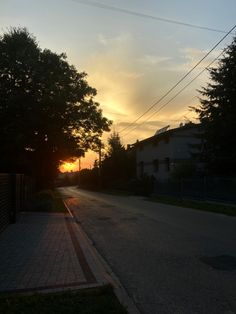 the sun is setting behind some trees on the side of the road in front of houses