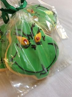 two decorated cookies wrapped in plastic sitting on a white tablecloth with green ribbon around the edges