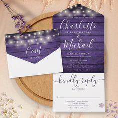 the wedding stationery is set on top of a wooden platter with purple flowers