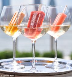 three wine glasses filled with different types of drinks on a tray outside in the sun