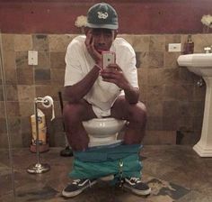 a man sitting on top of a toilet while holding a cell phone to his face