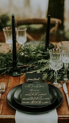 the table is set with black plates, silverware and greenery for an elegant dinner