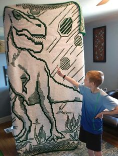 a young boy standing next to a giant knitted dinosaur blanket in a living room