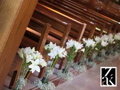 white flowers are in vases on the pews