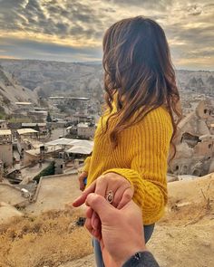 a woman holding the hand of a man on top of a hill with buildings in the background