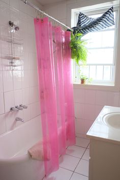 a pink shower curtain in a bathroom next to a white sink and window with potted plants