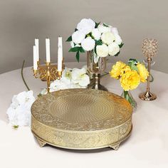 the table is set with white and yellow flowers in vases, candles, and plates