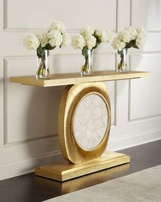 three vases with white flowers are sitting on a gold shelf in front of a wall