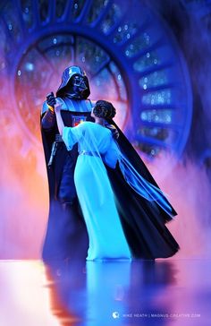 a man and woman dressed as darth vader and princess leisa hugging in front of a clock