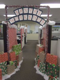 an office cubicle decorated for christmas with presents on the floor and santa's workshop sign