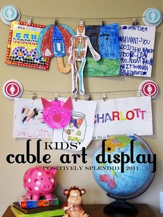 an art display with children's artwork hanging on the wall and toys sitting on top of it