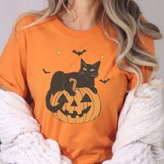 Nothing says Halloween like a classic black cat perched on a glowing jack-o'-lantern! This cute yet spooky design captures the essence of the season with a playful black cat, surrounded by twinkling stars and fluttering bats. Ideal for cat lovers who embrace the mystique and charm of black cats, this shirt is a must-have for your autumn wardrobe. This shirt's blend of a classic Halloween aesthetic and subtle witchy Halloween vibes makes it the perfect choice for anyone who loves to embrace a lit Spooky Cat Design T-shirt For Fall, Spooky Halloween T-shirt With Cat Design, Spooky Halloween Cat Design Top, At Home Halloween Costumes, Home Halloween Costumes, Lounge Party, Cat Mom Shirts, Black Cat Halloween, Cat Shirts