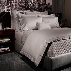 a bed with white sheets and pillows in front of a cityscape wallpaper