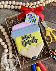 a decorated cookie in a box on a table with some crayons and markers