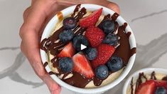 a person holding a bowl of fruit with chocolate sauce on top and strawberries in the bowl