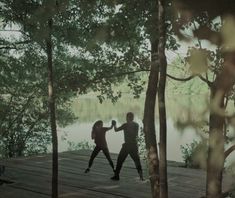 two people are dancing on a dock by the water in black and white photo with trees