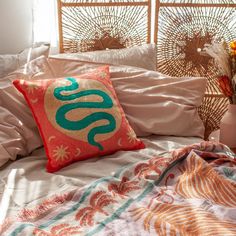 an orange and green pillow sitting on top of a bed next to a vase with flowers