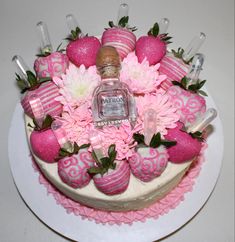 a cake decorated with pink flowers and strawberries is on a white plate, next to a bottle of booze