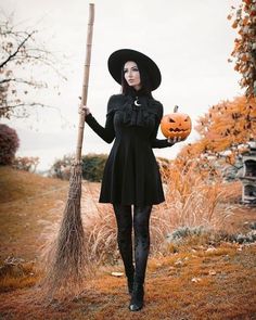 a woman in a black dress and hat holding a broom with a pumpkin on it