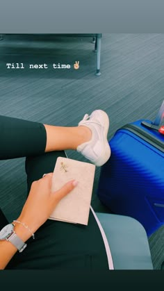 a woman sitting on the ground with her feet up next to a piece of luggage