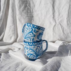 two blue and white coffee cups sitting on top of a bed covered in white sheets