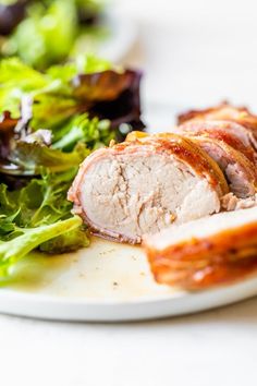 a white plate topped with meat next to a green leafy salad on top of a table