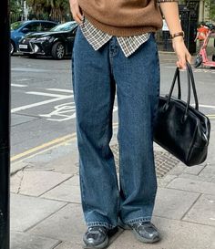 a woman is standing on the sidewalk with her hand in her pocket and holding a purse