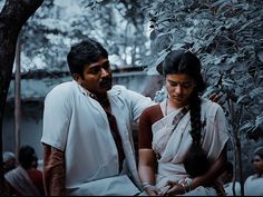 a man and woman sitting next to each other in front of a tree with lots of leaves