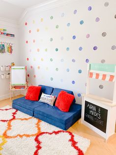 a blue couch sitting on top of a wooden floor next to a white wall covered in colorful polka dot decals