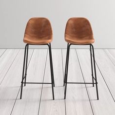 two brown leather stools sitting next to each other on a wooden floor in front of a white wall