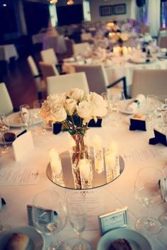 the table is set with white roses and candles for an elegant wedding reception or special event