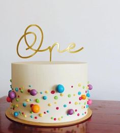 a white cake topped with colorful sprinkles and a gold one topper