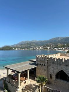 an old building sitting on top of a sandy beach next to the ocean with mountains in the background