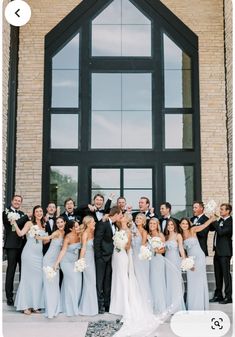 a large group of people standing in front of a building with their wedding party posing for a photo