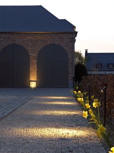 a brick building with two garages and yellow flowers in the foreground at dusk