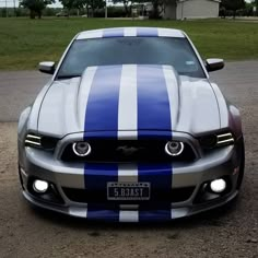 the front end of a blue and white striped mustang parked in a parking lot next to a house