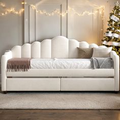 a white daybed sitting in front of a christmas tree with lights on the wall