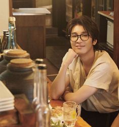 a woman wearing glasses sitting at a table with food and drinks in front of her