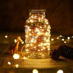 a mason jar filled with fairy lights sitting on top of a table next to a pine cone