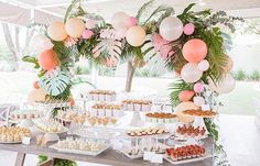 a table filled with lots of desserts under a white tent covered in palm leaves