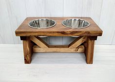 two stainless steel bowls sit on top of a wooden table with white wall in the background