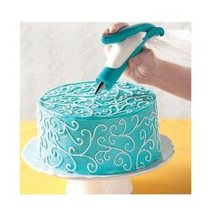 a person is using a pen to decorate a blue cake with white swirls on it