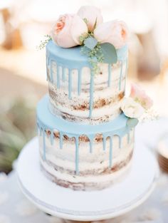 a three tiered cake with blue icing and pink flowers on the top layer