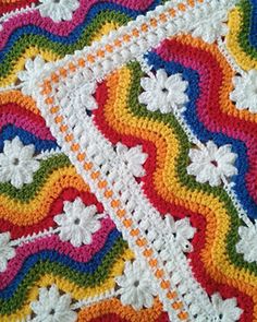 a crocheted blanket with white flowers and rainbows in the center, on top of a table