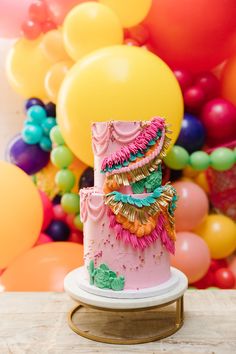 a pink cake sitting on top of a wooden table next to balloons and streamers