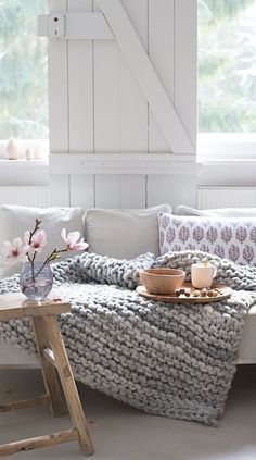 a white couch sitting next to a wooden table in a living room under a window