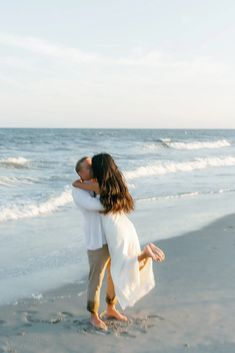 a man and woman kissing on the beach next to the ocean with waves coming in